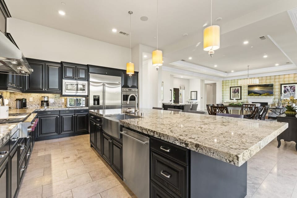 Modern kitchen w/ large granite island, dark cabinetry & pendant lighting