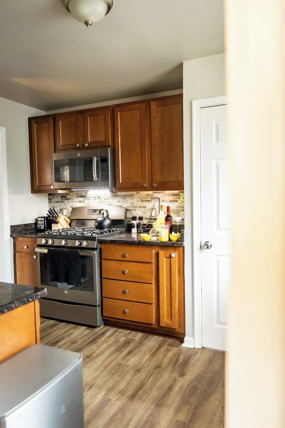 This modern kitchen features stainless steel appliances, rich wood cabinetry, and sleek granite countertops. With a gas range, microwave, and stylish backsplash, it’s fully equipped for cooking meals or enjoying a relaxing night in with food & drink.