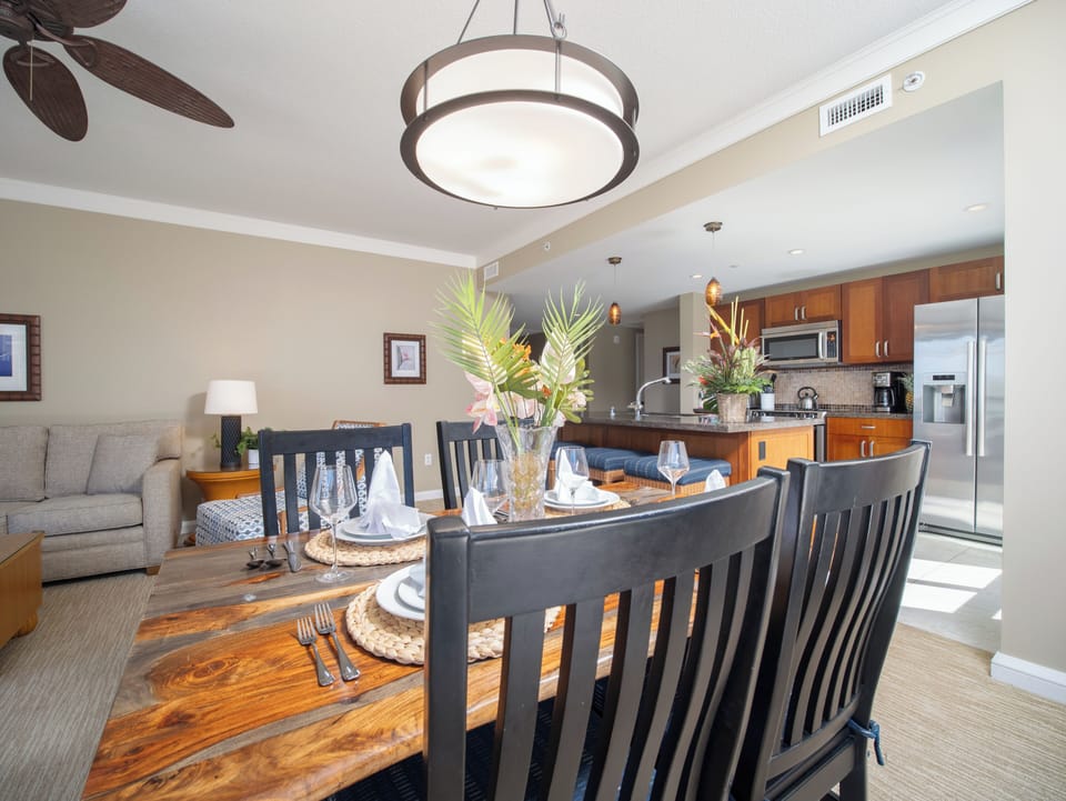 Dine in style with this elegant wooden dining table, complete with tropical floral decor, set next to the open kitchen.
