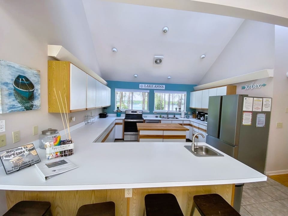 A spacious kitchen with a large island, barstools, and modern appliances with scenic lake views through the window.