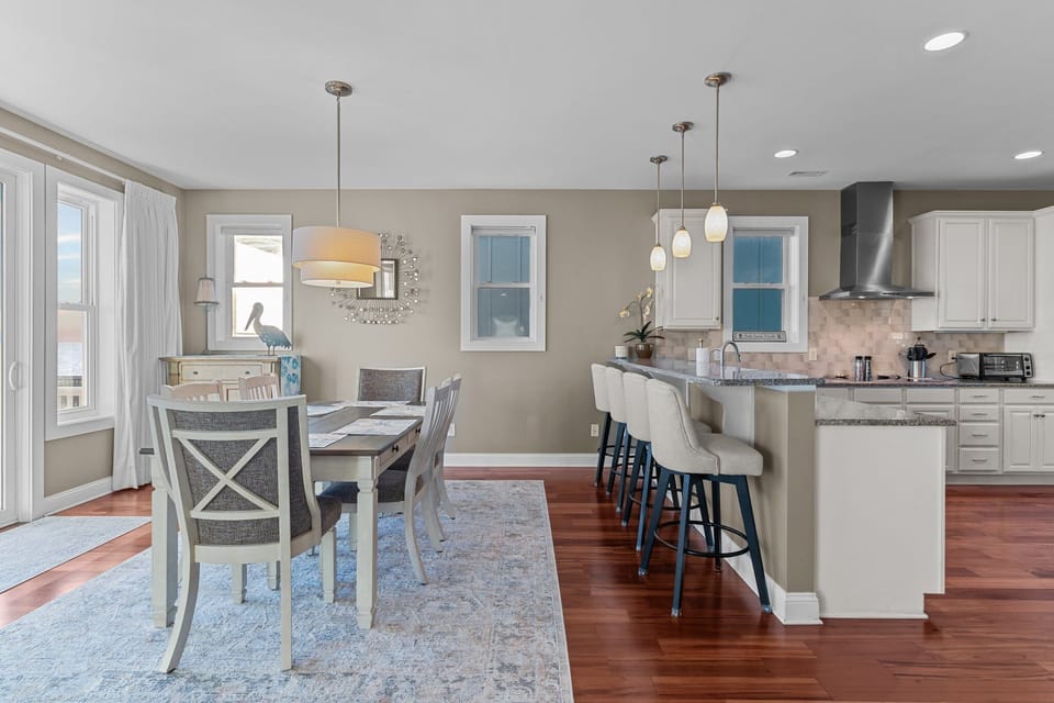 Bright coastal kitchen with white cabinets, double wall ovens, granite counters, stainless appliances, pendant lights, hardwood floors, and ocean views beyond the sink.