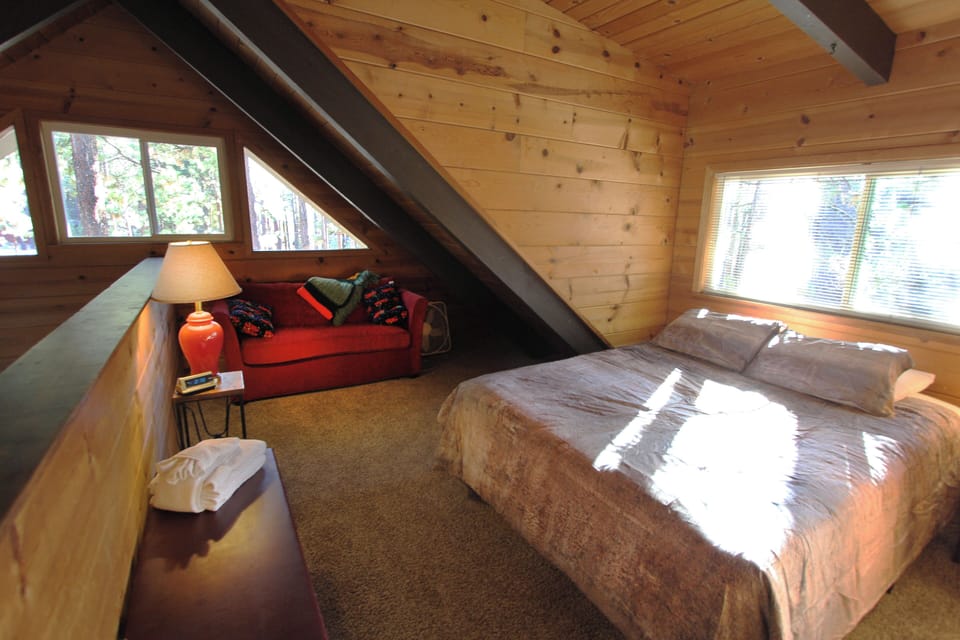 Loft with bed, sofa, side table, lamp, windows, railing, and folded towels.
