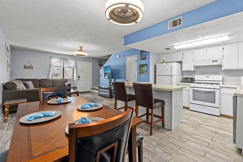 A kitchen with a sleek breakfast bar, open to the dining room opens to the living room, featuring a bold blue accent wall for a pop of color.
