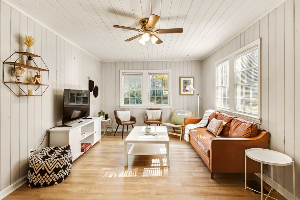 Bright and cozy living room with a stylish leather sofa and ample natural light, perfect for relaxation.