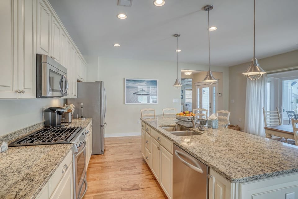30220 Seaglass Way - Contemporary Kitchen Craftsmanship - This perspective highlights the professional-grade gas range and built-in microwave, complemented by elegant pendant lighting over the island. Rich hardwood floors provide a warm contrast to the bright, modern finishes.