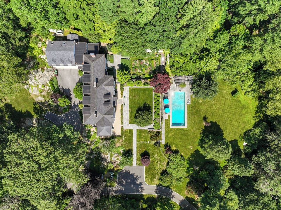 This aerial view showcases the estate’s stunning layout—featuring lush gardens, a sparkling pool, and expansive grounds perfect for family fun and relaxation. A true luxury retreat surrounded by nature and privacy.