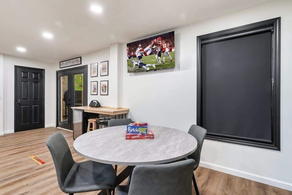 Modern dining area with a round table, board games, and a wall-mounted television for entertainment.