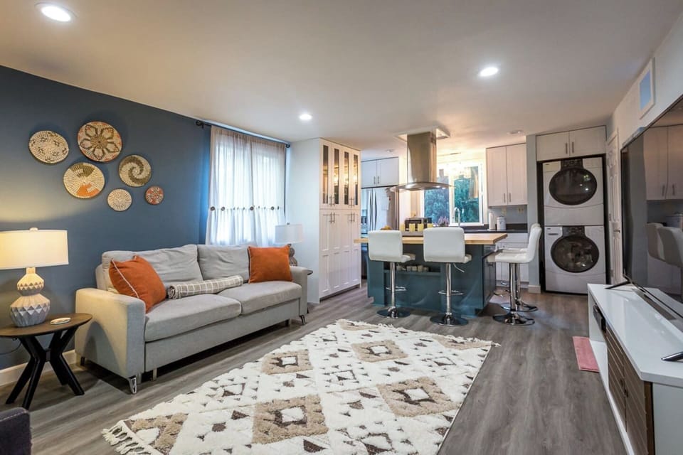- Stylish open living area with blue accent wall and cozy gray sofa seating  
- Modern kitchen with breakfast bar seating for four and full appliances  
- Includes in unit washer and dryer for guest convenience during stays  
