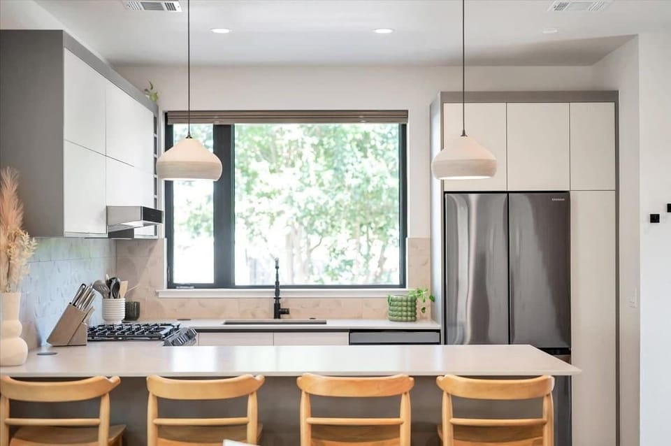 Kitchen view from the living area. Beautiful matte stone counters, custom handmade ceramic pendants, dimensional tile backsplash, pop up outlets. Baby seat that hooks to the counter available.