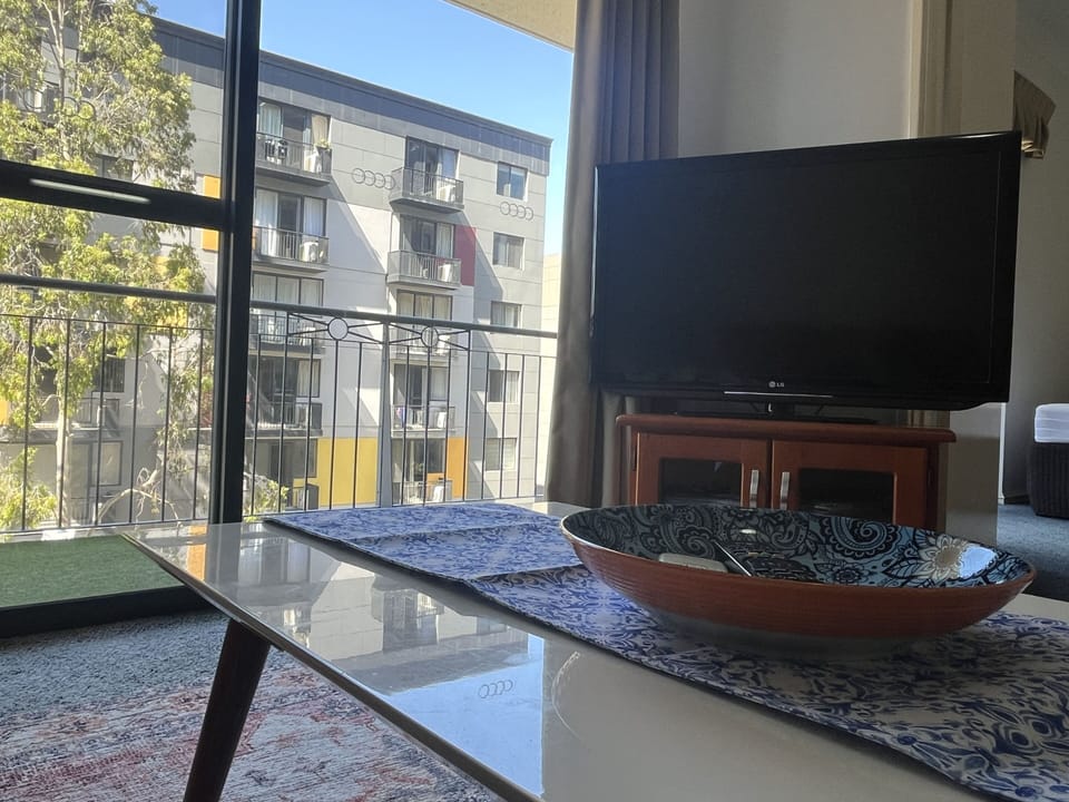 This comfortable living room features a TV for entertainment, a cozy carpet, and direct access to the balcony, with a convenient living room table for your use, offering a seamless indoor-outdoor experience.