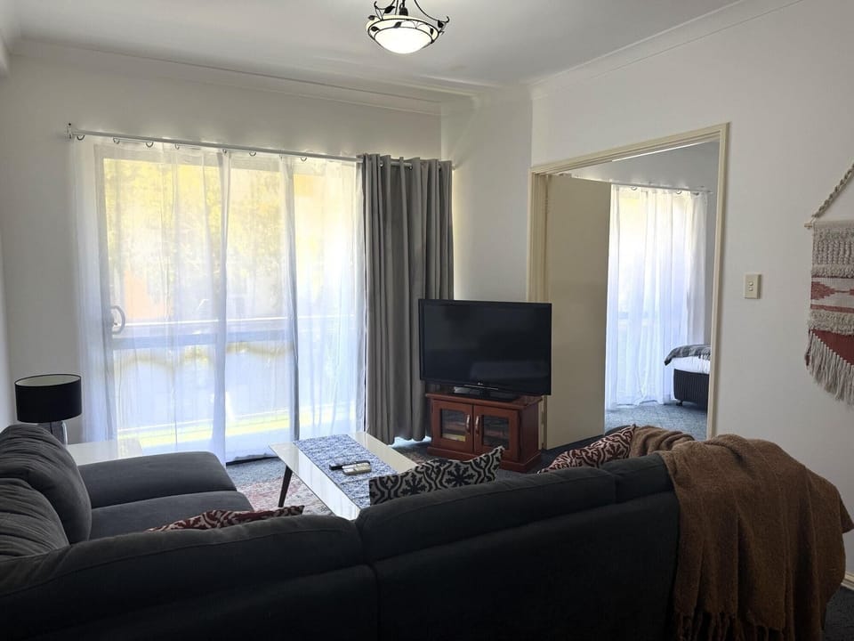 This inviting living room features a comfortable sofa, a practical table, and soft carpet, all with a TV for your entertainment. Conveniently located close to the balcony for seamless indoor-outdoor living.
