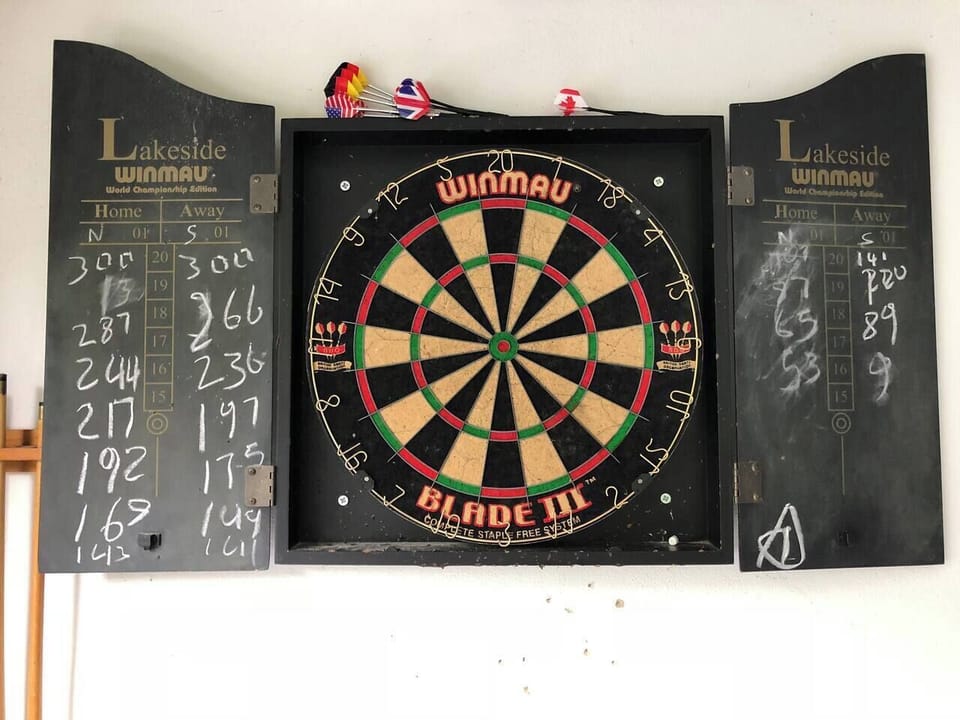 Dart board with several sets of darts in the games room