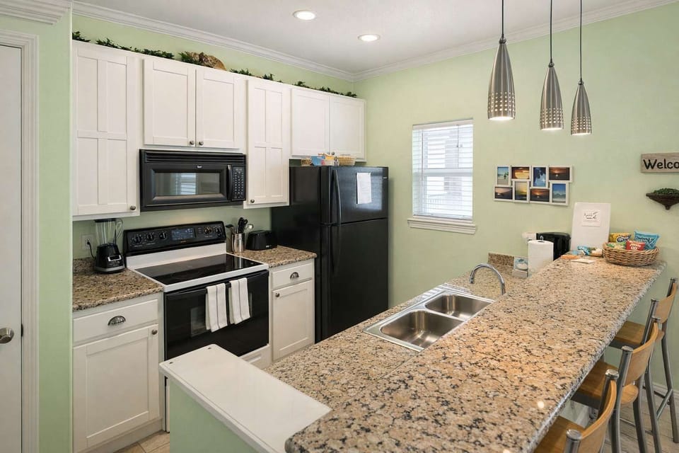 Bright, modern kitchen with granite countertops, stainless steel sink, black appliances, and pendant lighting—perfect for cooking, entertaining, or enjoying a morning coffee at the breakfast bar.