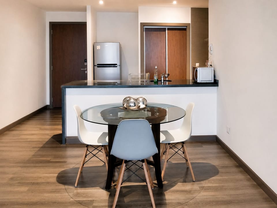 Enjoy meals or catch up on work at the modern dining area, complete with a stylish glass table and seating for four. Conveniently located next to the fully equipped kitchen, it offers a comfortable and functional space for any stay.