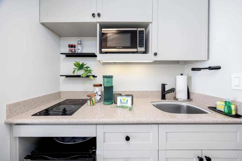 This well-appointed kitchenette features modern white cabinetry, a convenient two-burner stovetop, microwave, sink, and essential appliances like a Keurig coffee maker, perfect for light meal preparation.