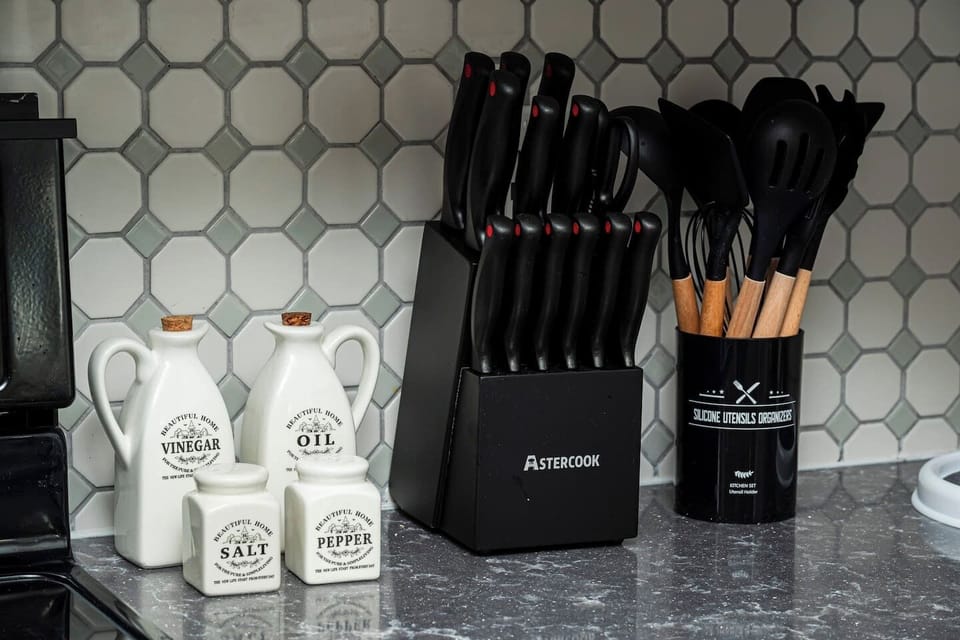 A well-equipped kitchen counter with essential cooking tools organized neatly. There's a knife block holding a set of sharp knives, a utensil holder with wooden spoons and spatulas, and containers for salt, pepper, oil, and vinegar.