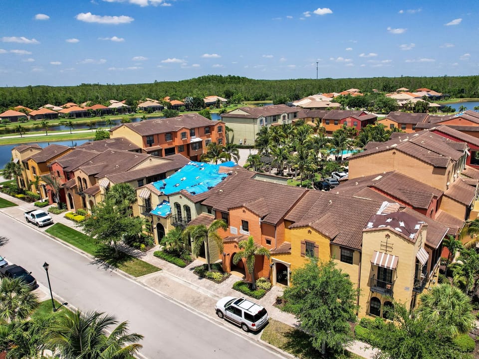 Colorful townhouses with tiled roofs surround a central pool area in a sunny residential community.