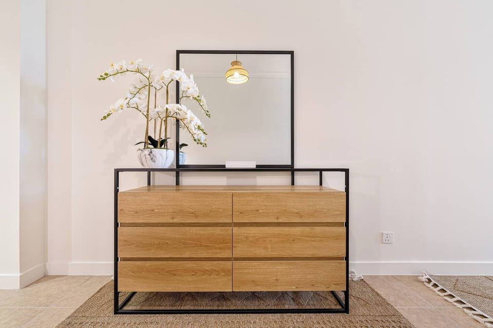 Bedroom includes a functional console cabinet and a large wall mirror, combining style with practicality.
