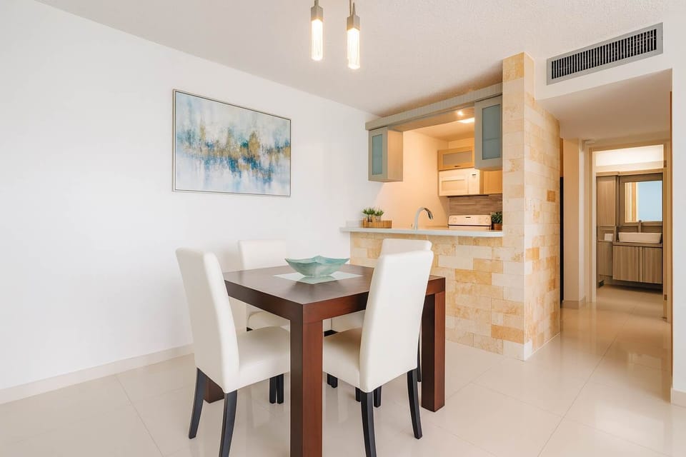 Bright dining area with a modern touch—features a sleek wooden table, soft lighting, and an open kitchen design. Perfect for enjoying meals in a cozy, stylish setting.