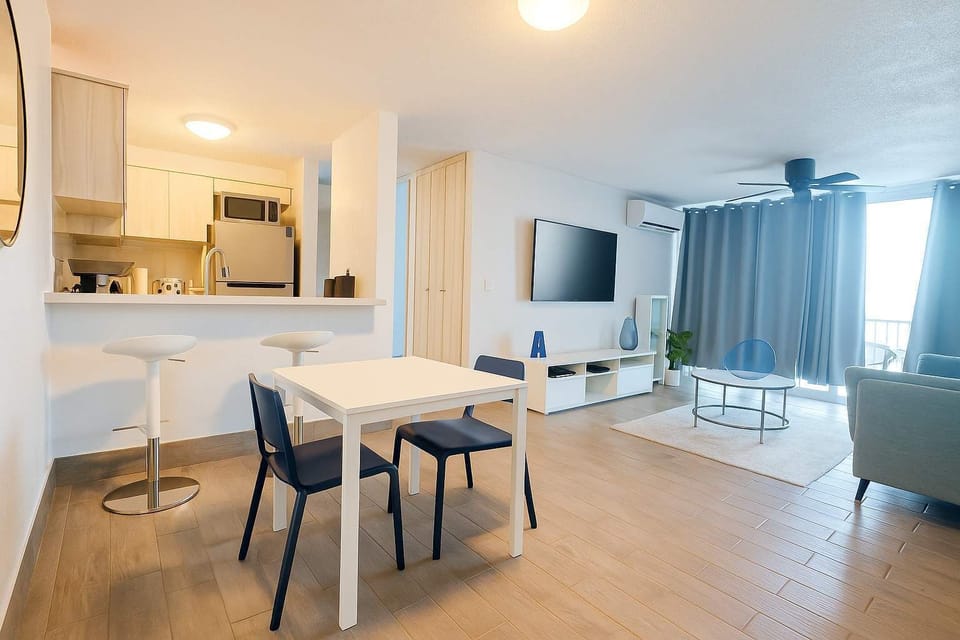 Modern open-concept living space featuring a cozy seating area, flat-screen TV, and bright dining nook. The fully equipped kitchen and inviting layout make it perfect for relaxing or entertaining after a beach day.