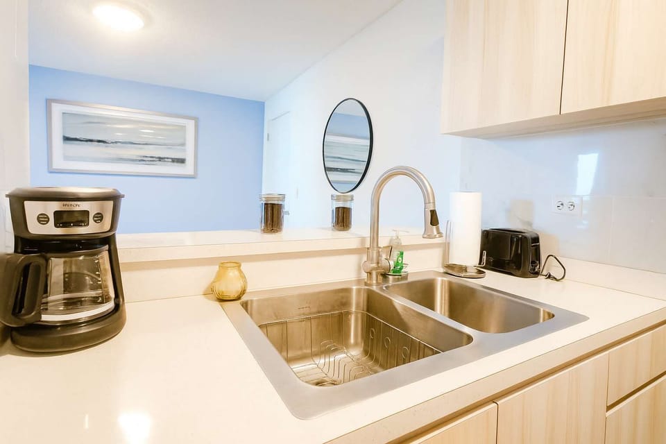 Bright and functional kitchen featuring sleek countertops, stainless steel sink, and modern appliances. Perfect for brewing your morning coffee or preparing a quick island meal.