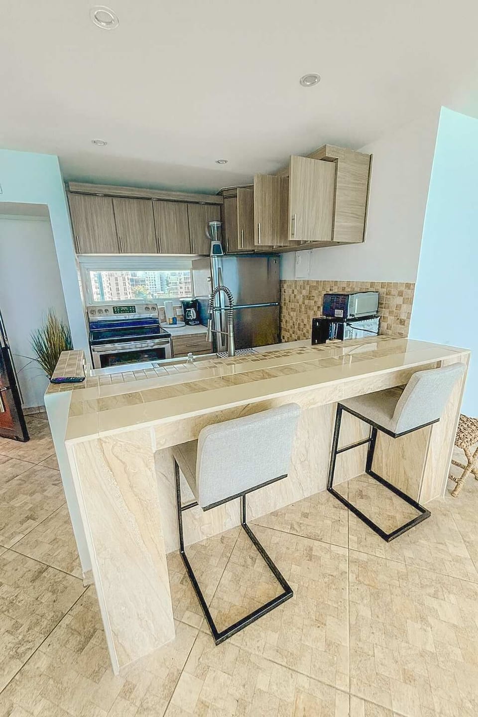 Bright and modern kitchen with stainless steel appliances, marble-style counters, and cozy bar seating — ideal for cooking or casual dining.