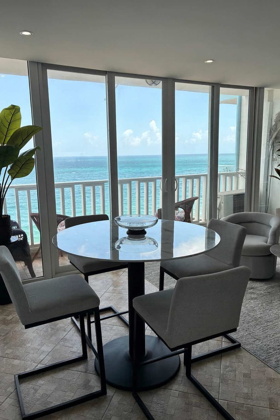 Ocean-view dining area with sleek modern furniture and full glass windows — a bright, elegant space perfect for seaside breakfasts or sunset dinners.