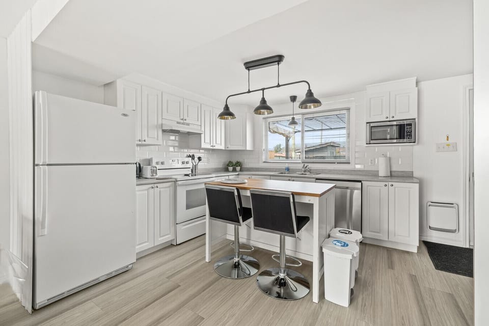 6:29 PM Bright, fully-equipped white kitchen with stainless steel appliances, a central island with seating for two, and stylish pendant lighting.