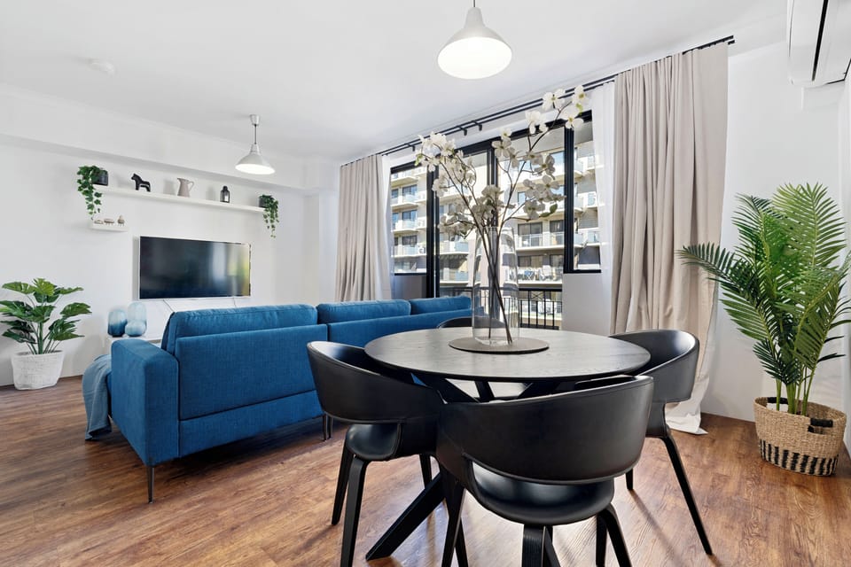 Enjoy meals in a modern dining room complete with a dining table and chairs, a blue couch, and a large window.