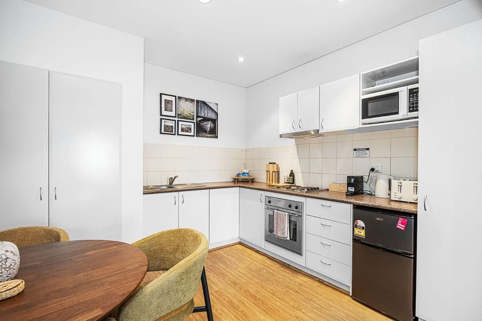 Prepare meals in a compact yet functional kitchen featuring white cabinetry, modern appliances, and a tiled backsplash, offering an efficient space for cooking and daily tasks.