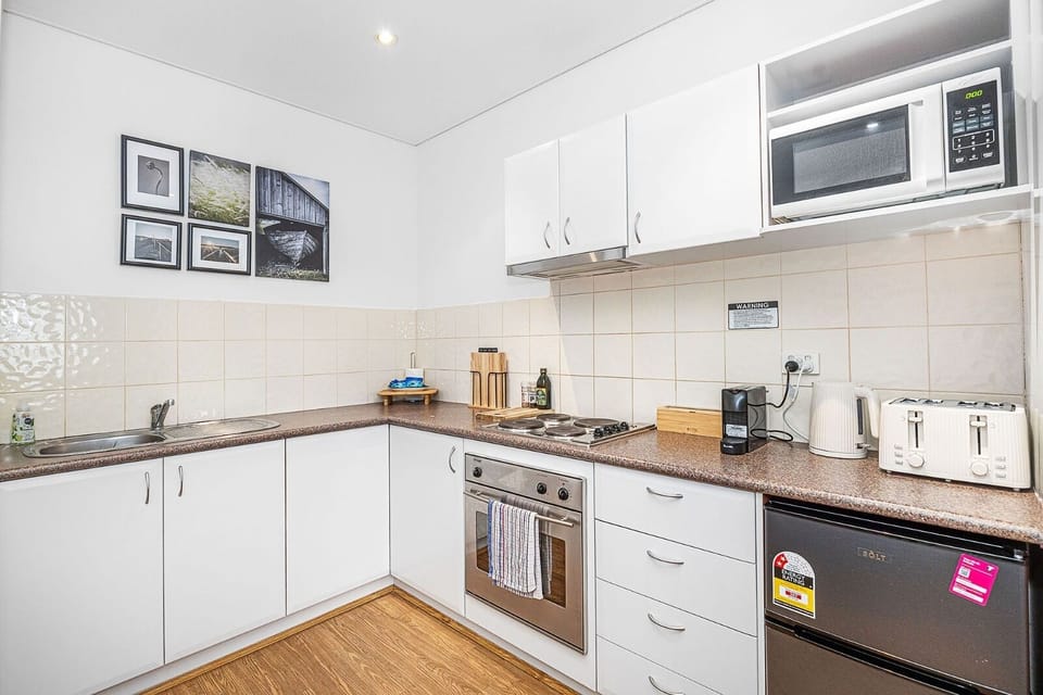Prepare meals in a compact yet functional kitchen featuring white cabinetry, modern appliances, and a tiled backsplash.