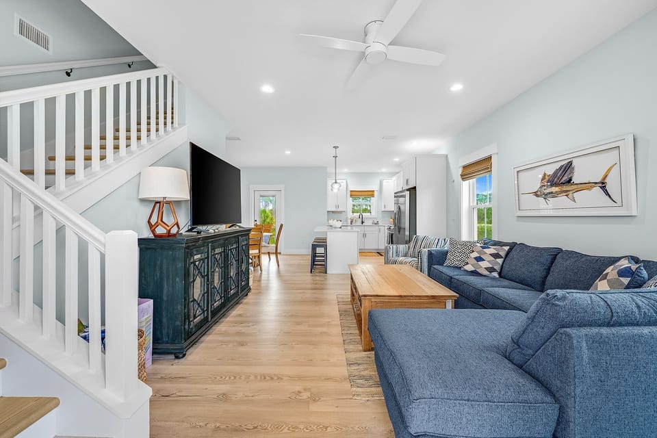 Sink into plush navy sofas in your open-concept living space, where coastal charm meets modern comfort beneath soaring ceilings.