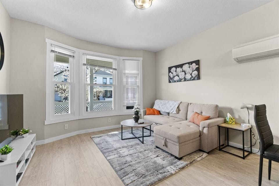 Bright and inviting living room with a sectional sleeper sofa and three oversized windows that flood the space with natural sunlight.