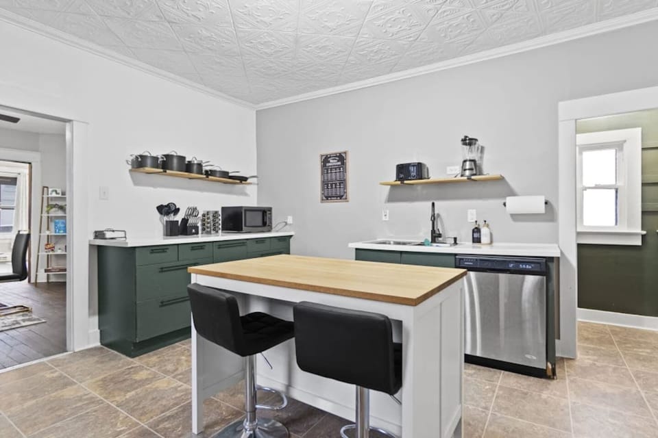 Stylish full kitchen featuring a long table with a chair, sink with faucet, microwave, cozy flooring, and a functional divider leading to the dining area—combining practicality and modern elegance for a warm, inviting space