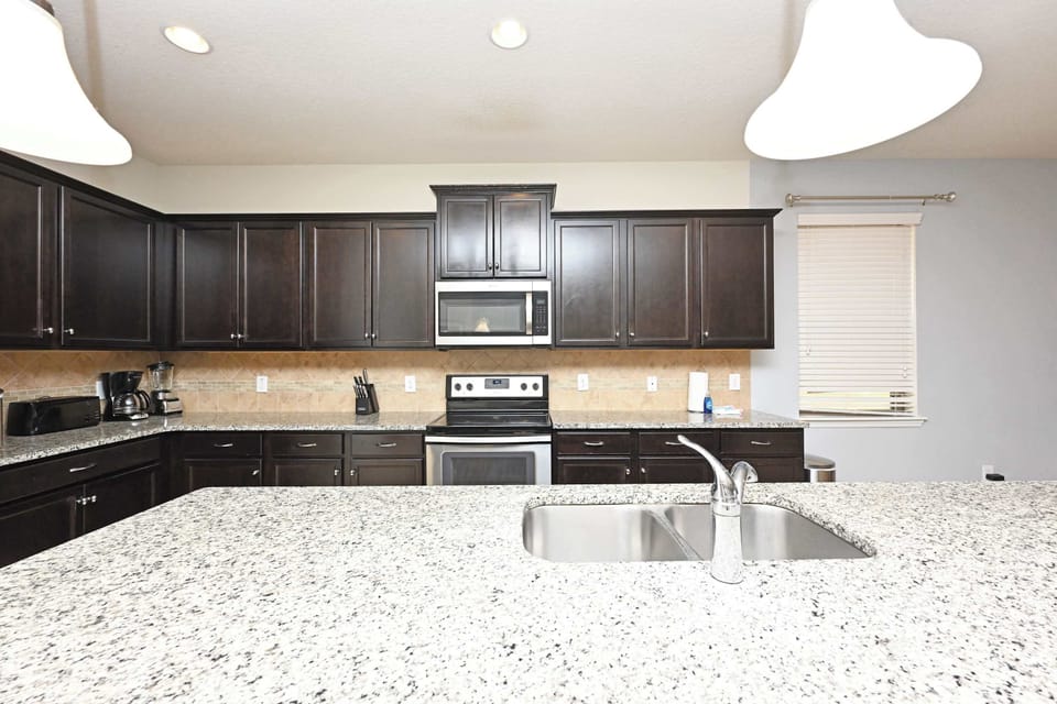 Modern kitchen with dark wood cabinets and granite countertops featuring a double sink and stainless steel appliances.