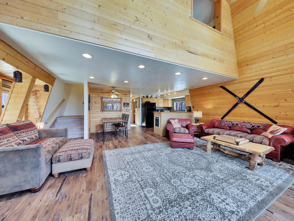 Great room featuring expansive tree views, access to an outdoor deck with a seating area, a cozy wood-burning fireplace, ceiling fans for added comfort, board games, a 43" Smart TV, and plush, comfortable seating.