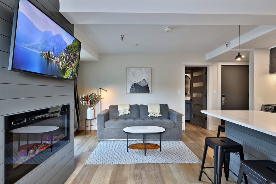 Settle onto the sofa with the television and wall fireplace ahead and the kitchen island just behind you.