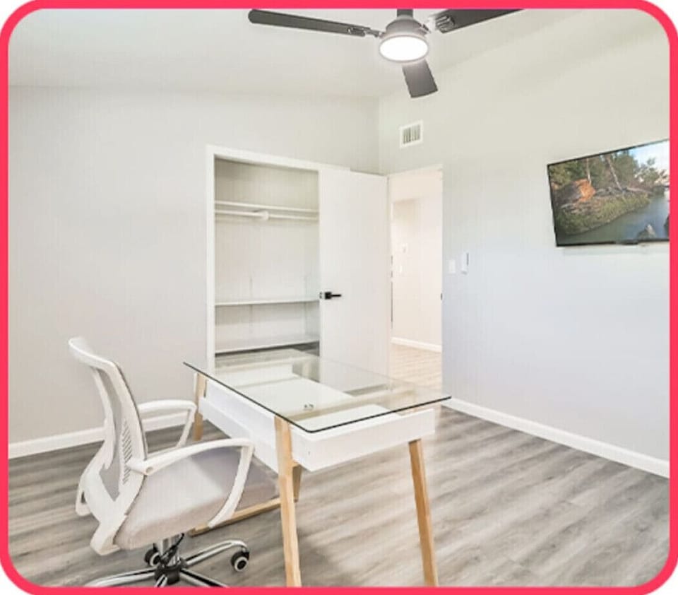 Functional office nook featuring a glass-top desk, ergonomic chair, built-in closet shelving, and a wall-mounted TV.