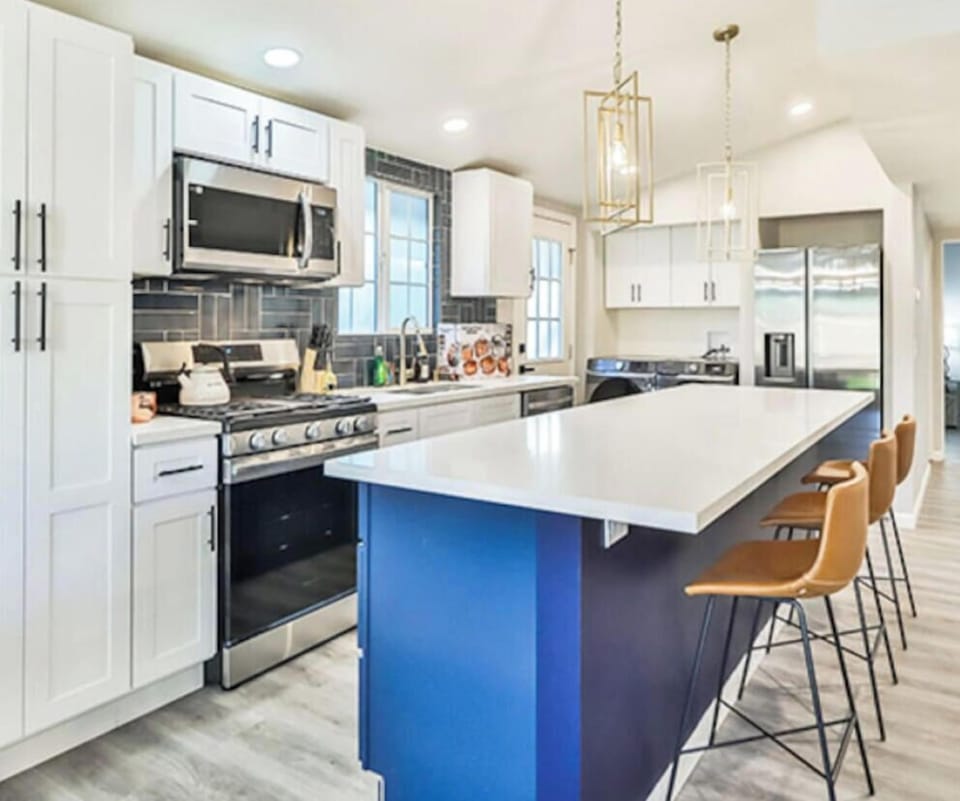 Gourmet kitchen featuring white shaker cabinetry, stainless steel appliances, a large navy blue island with a breakfast bar, and designer pendant lighting.