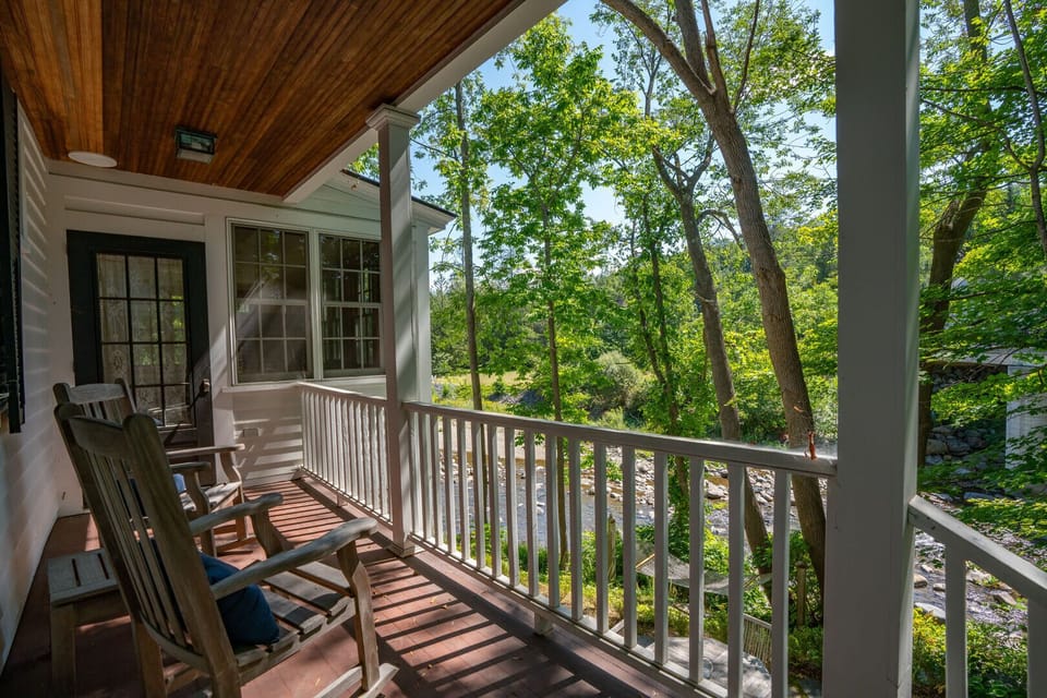 Covered porch with rocking chairs and river views through the trees