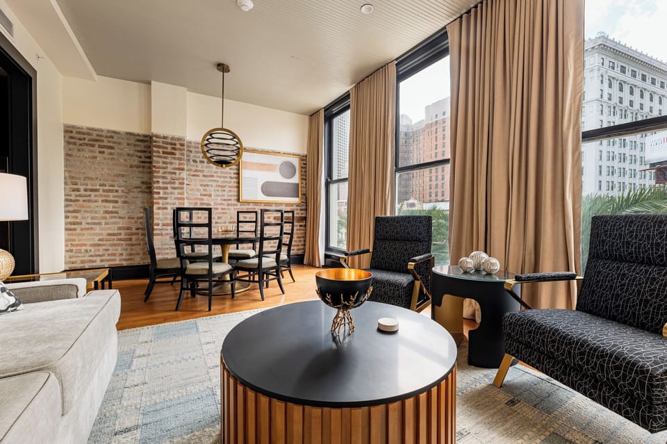 A stylish living and dining space highlighted by exposed brick and natural light from large windows overlooking a bustling cityscape.