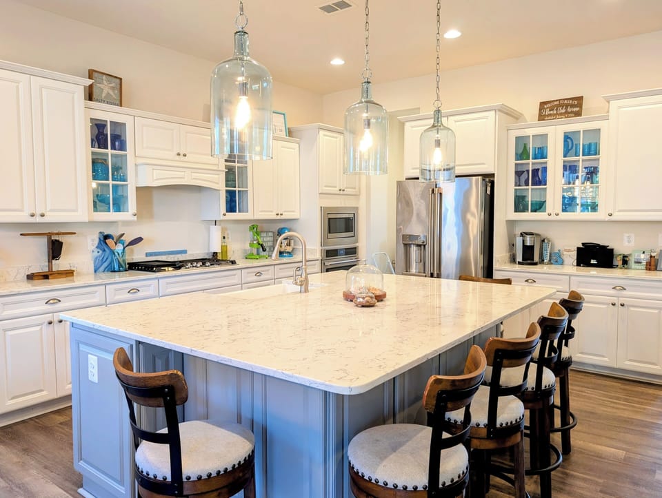 51 Beach Club Avenue - Gourmet Kitchen - Stunning chef's kitchen featuring a massive light blue center island, white cabinetry with glass inserts, stainless steel appliances, and chic pendant lighting.