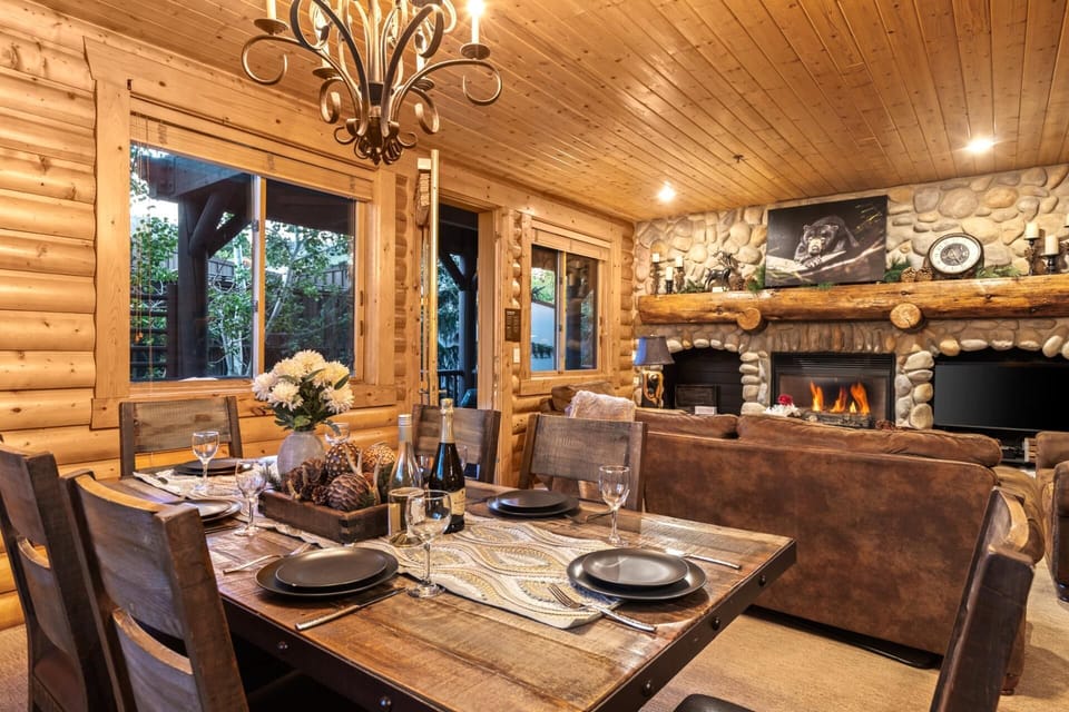 Rustic dining space with log walls, chandelier, and forest views.