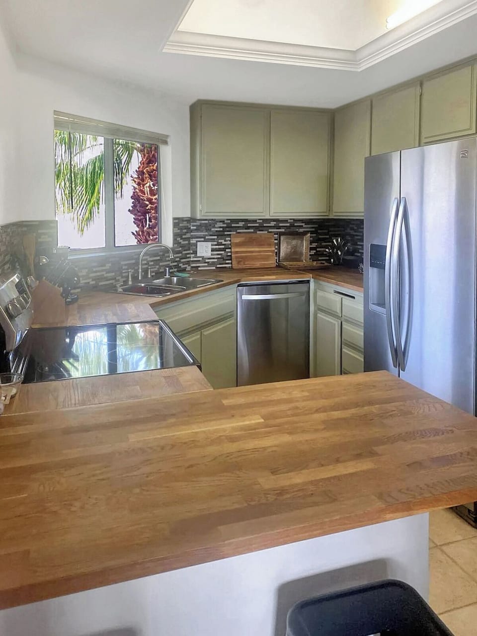 Bright kitchen with wood counters, stainless stove,mosaic backsplash window view
