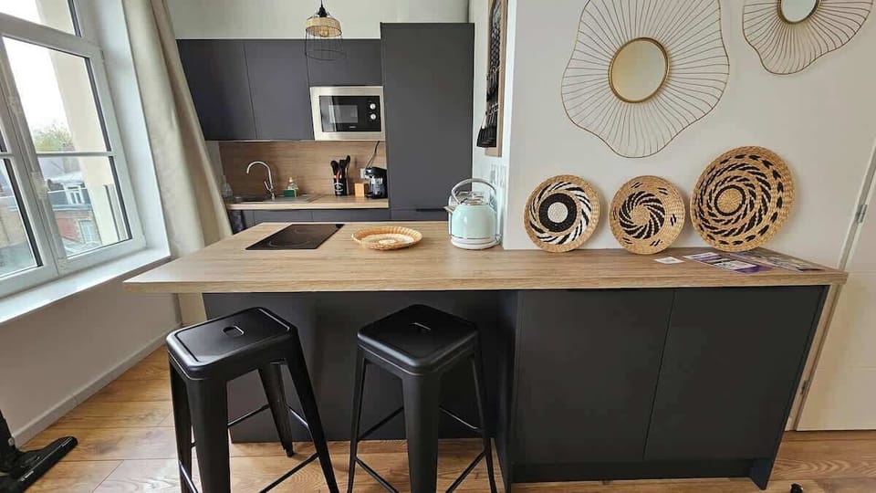 Cuisine, ouverte sur le salon, équipée avec un petit réfrigérateur derrière une porte de placard, un four de l'autre côté du plan de travail, un lave-vaisselle, un micro-ondes et une machine à café. 
Coin repas "sur le pouce" grâce aux deux tabourets