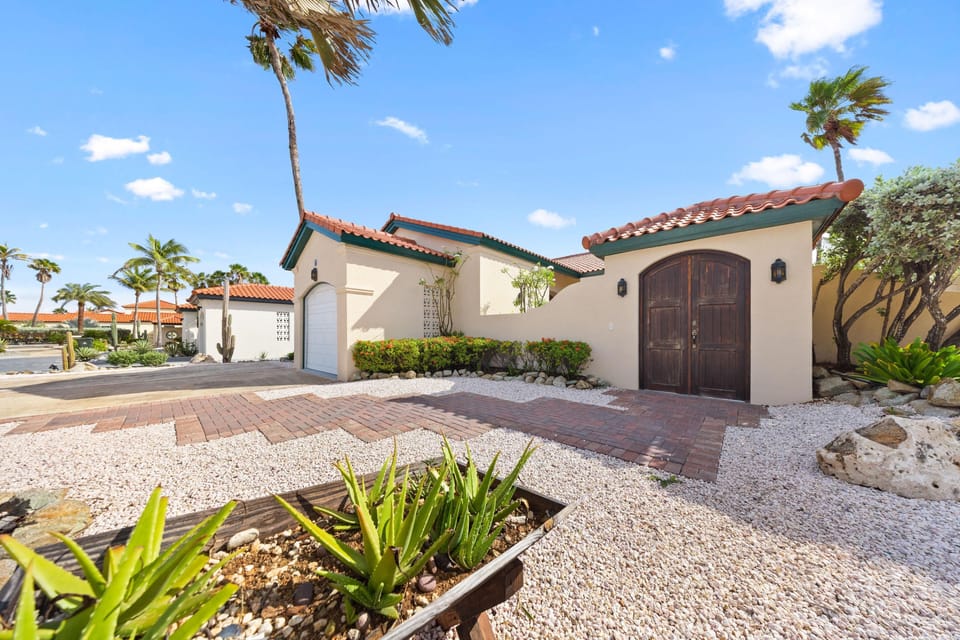 Tropical-style home with a well-kept courtyard, paved pathway leading to a double wooden door, and parking.