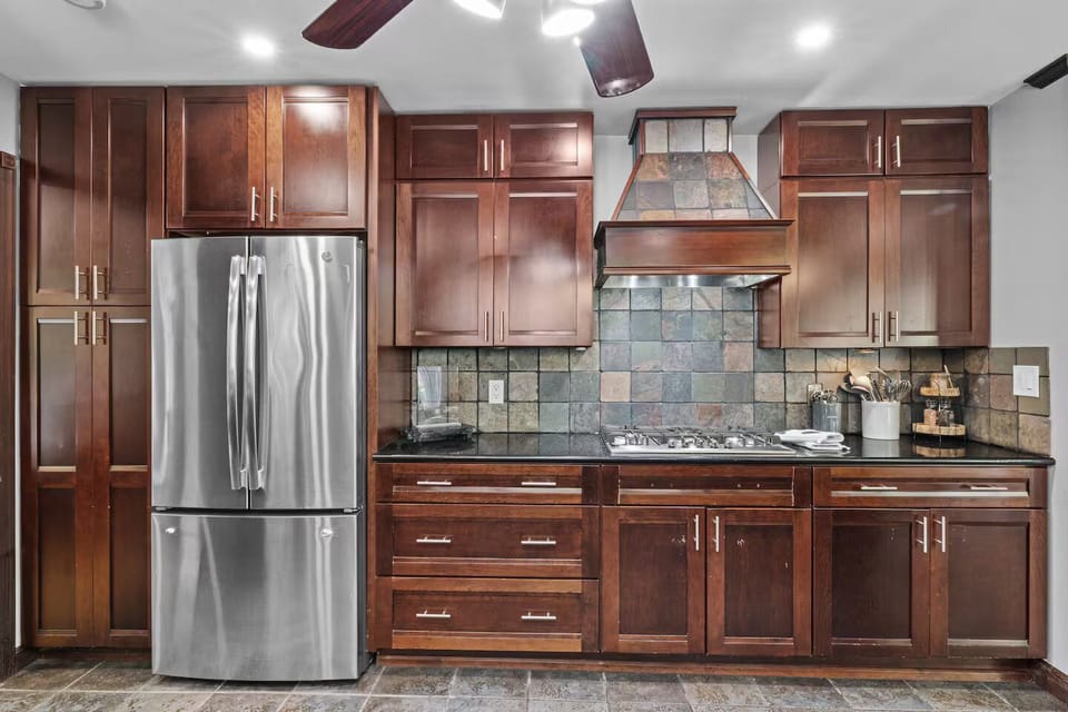 Modern full kitchen with rich wood cabinetry, granite counters, and bar seating.