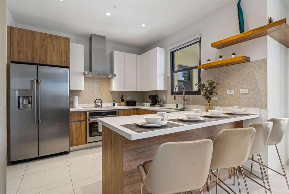 - Cook in style with this sleek, modern kitchen featuring appliances and a spacious island - Clean lines, wood accents, and open shelving create a functional yet inviting space - Designed for cooking, dining, and making unforgettable memories