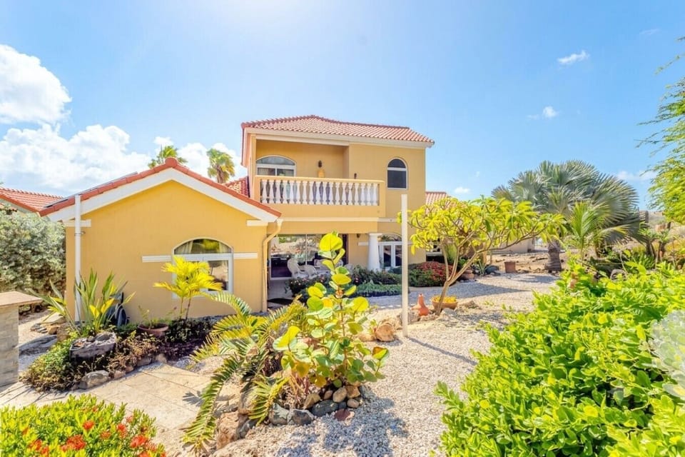 A large yellow house with a tile roof and a gravel yard.