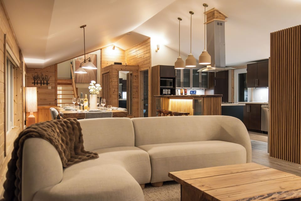 Cozy up in this inviting open-concept living space. Warm wood tones and soft lighting create a relaxing atmosphere. Gather around the fireplace and dining table, or unwind on the plush seating. The perfect space to connect with loved ones.